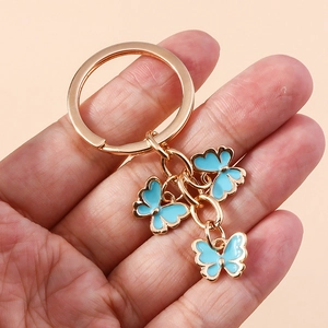 Detailed close-up of golden metal keychain with three light blue butterfly enamel charms