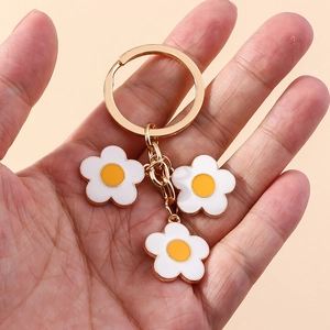 Detailed macro view of gold keychain with three white and yellow enamel daisy pendants