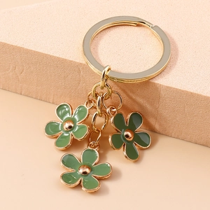 Detail of green enamel cherry blossom charms and golden metal keyring on a textured block