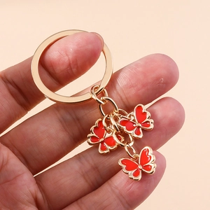 Detailed close-up of golden keychain with three vibrant red enamel butterfly pendants