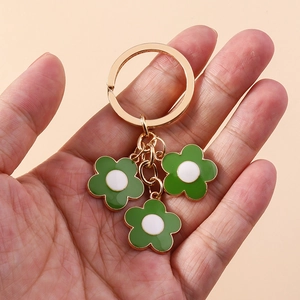 Detailed close-up of a golden keychain featuring three green enamel flowers with white centers