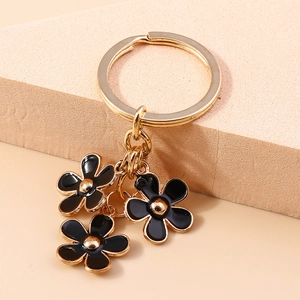 Detail of three black enamel flower charms on a polished golden metal keychain