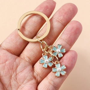 Détail d'un porte-clés en alliage doré avec trois fleurs bleu clair et perles blanches