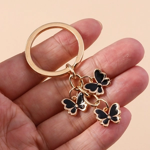 Golden butterfly keychain with three black enamel charms held against a pink background