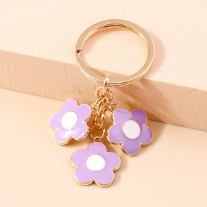 Close-up of golden keychain featuring three purple cherry blossom flower charms on a beige stone