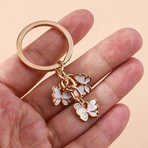 Gold-plated butterfly keychain with white enamel charms held against a plain orange background