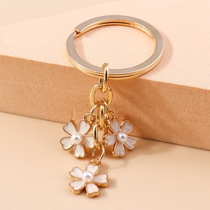 Vue détaillée du porte-clés doré avec fleurs en émail blanc et perles centrales