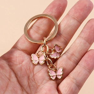 Golden keychain featuring three pink enamel butterfly pendants held by a hand