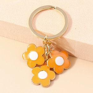 Detailed macro view of gold keychain with three orange enamel floral pendants