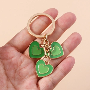 Porte-clés minimaliste doré avec pendentifs cœurs en émail vert tenu en main