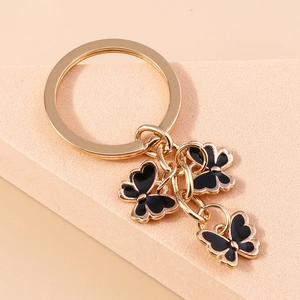 Close-up of golden keychain with three black enamel butterflies on a soft pink stand