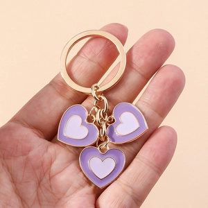 Gros plan d'une main tenant un porte-clés doré avec trois cœurs en émail violet