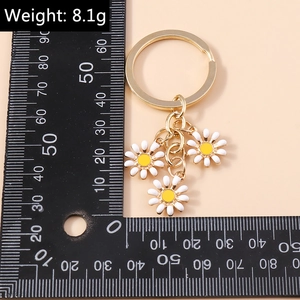Dettaglio portachiavi a margherita con anello in metallo dorato e tre ciondoli floreali