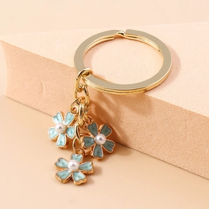 Détail du porte-clés à fleurs en émail bleu et perles blanches sur anneau en métal doré