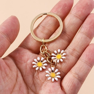 Portachiavi con margherita tenuto in mano con tre fiori di smalto bianco e anello oro
