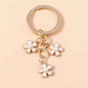 Détail d'un porte-clés doré avec fleurs en émail blanc et perles nacrées au centre