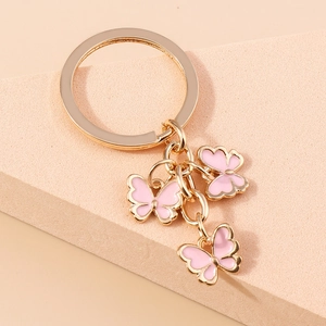 Detail of gold keychain featuring three pink enamel butterfly charms on a textured base