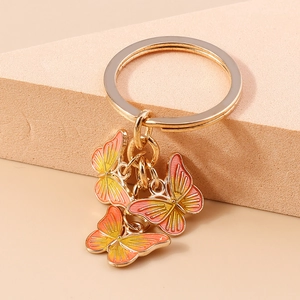 Détail macro de trois breloques papillons en émail dégradé orange sur un porte-clés doré
