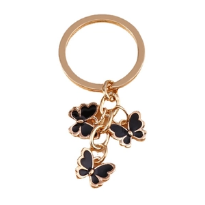 Golden butterfly keychain with three black enamel charms on a minimalist white background
