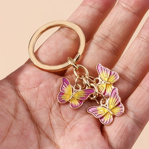 Détail macro de trois papillons en émail dégradé rose et jaune sur un porte-clés doré