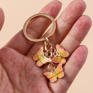 Main tenant un porte-clés doré avec trois pendentifs papillons en émail dégradé orange