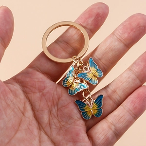 Porte-clés papillon doré avec breloques en émail dégradé bleu et jaune tenu à la main
