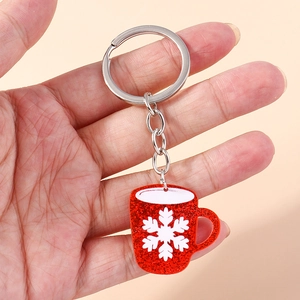 Close-up of a red glitter Christmas mug keychain with a white snowflake on a pink background