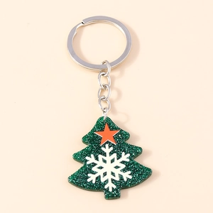 Detail of green glitter Christmas tree keychain with white snowflake and orange star