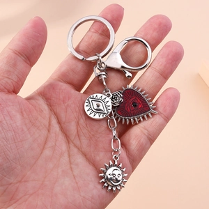 Detail of silver alloy keychain with red heart eye and mystic sun charms held in hand