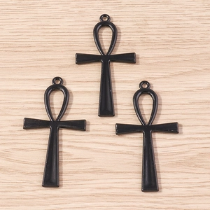 Vue détaillée de trois pendentifs croix Ankh noirs avec anneaux sur fond en bois