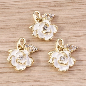 Detailed close-up of three gold rose flower pendants with white enamel and sparkling crystals