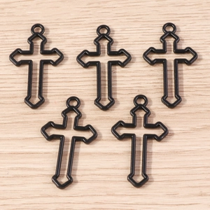 Détail de cinq breloques croix noires en alliage sur fond de bois clair pour bijoux