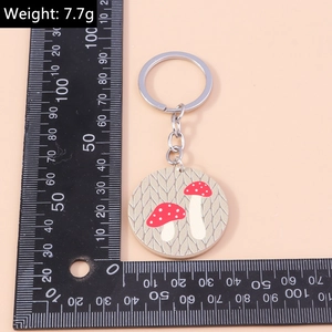 Détail d'un porte-clés en acrylique à motif champignon avec anneau argenté sur règle