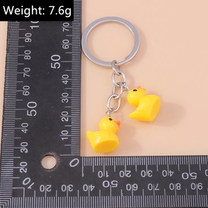 Weight 7.6g double little yellow duck keychain with silver alloy ring on pink surface