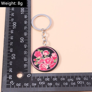 Mesure d'un porte-clés rond noir avec motifs de roses roses, pesant environ 8 grammes