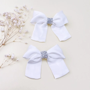 Dettaglio di fiocchi per capelli in raso bianco con strass e perle per bambine