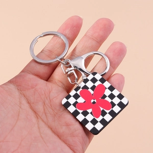 Détail d'un porte-clés à damier avec fleur rouge tenu à la main sur fond neutre