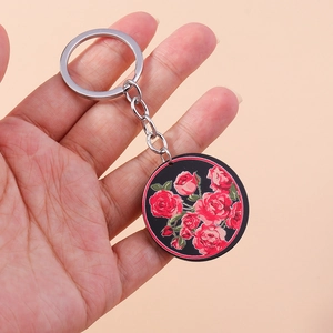 Porte-clés vintage rond tenu en main avec motif de roses rouges sur fond noir