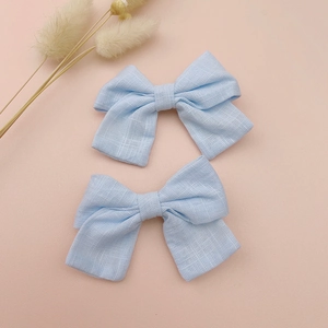 Close-up of two light blue linen bow hair clips on a soft pink textured background