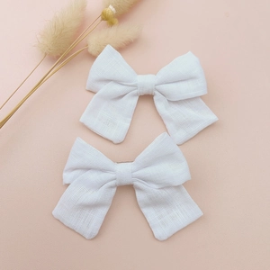 Close-up of a pair of handmade white linen bow hair clips on a soft pink background