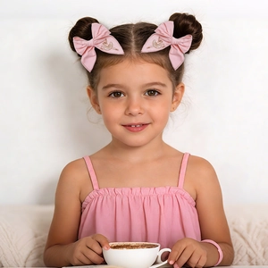 Pink bow hair clips featuring gold ballerina embroidery worn by a young girl