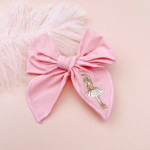 Detail of pink fabric bow hair clip with intricate ballet girl embroidery and soft cotton texture