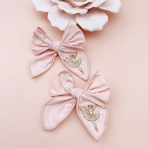 Close-up of pink fabric bow hair clips with gold ballet dancer embroidery detail
