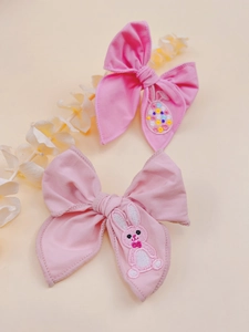 Close-up of pink bow hair clips with ballet bunny and rainbow egg embroidery details