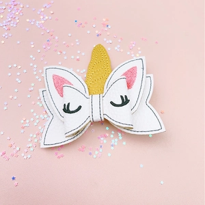 Close-up of embroidered unicorn bow hair clip with gold horn and pink glitter details
