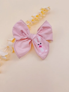 Detailed view of pink bow hair clip with cute rabbit embroidery on soft cotton fabric