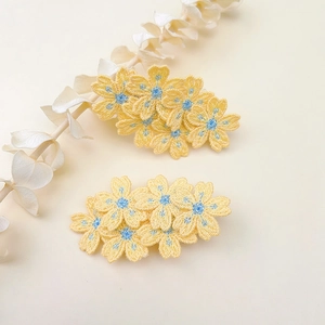 Detail of yellow floral embroidery hair clips with delicate blue centers and high texture