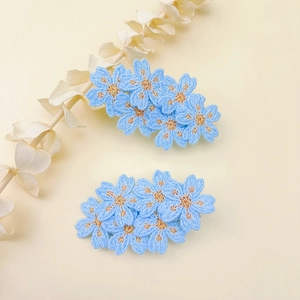Detailed macro view of two blue floral embroidered hair clips with gold thread centers