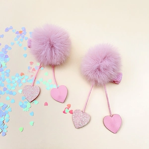 Détail de barrettes à pompons roses avec pendentifs en cœur pailleté et pinces en tissu