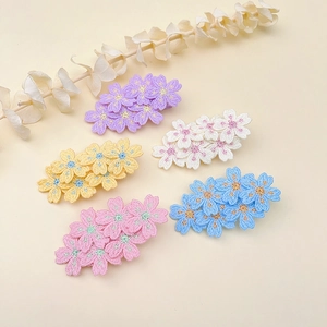 Floral embroidered hair clips in five colors displayed on a beige background with dried flowers
